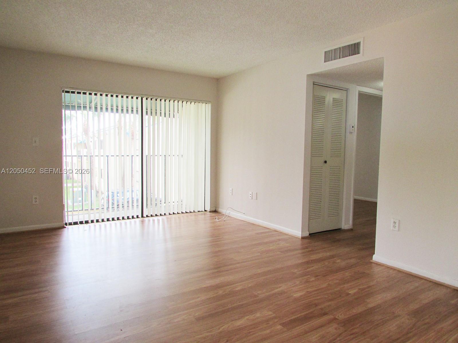 An empty living room features wood-look flooring, a sliding glass door, and a closet — 7407 SW 152nd Ave # 204, Miami FL 33193, MIAMI, FL