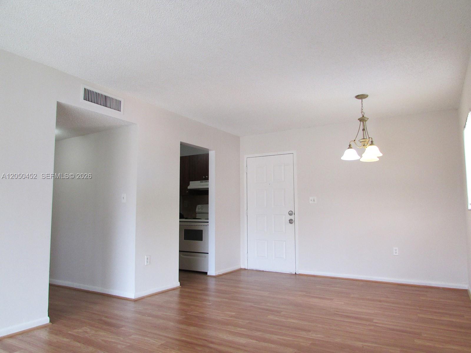 An interior view of a dining area with wood-look flooring, a chandelier, and a kitchen doorway — 7407 SW 152nd Ave # 204, Miami FL 33193, MIAMI, FL