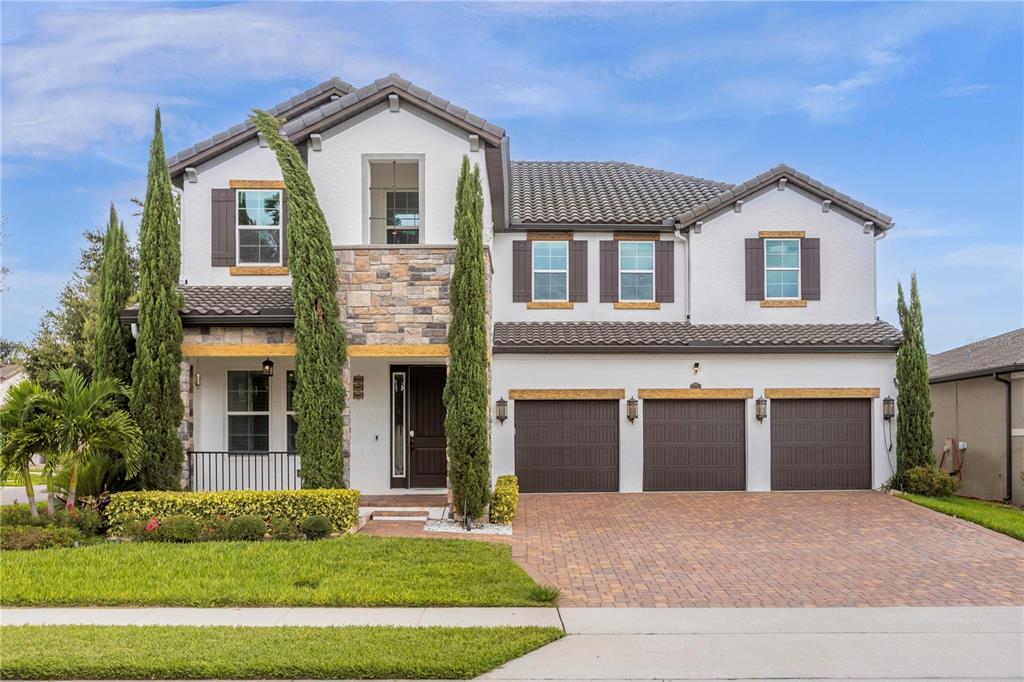 A two-story house with a stone facade, white stucco, three garage doors, and tall cypress trees — 1734 AMSEL FALLS PARK TERRACE, WINTER GARDEN, FL