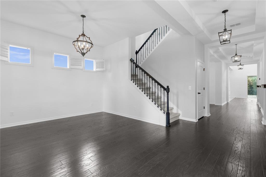 A bright foyer features a staircase with black railings, two cream armchairs, and dark flooring — 1734 AMSEL FALLS PARK TERRACE, WINTER GARDEN, FL