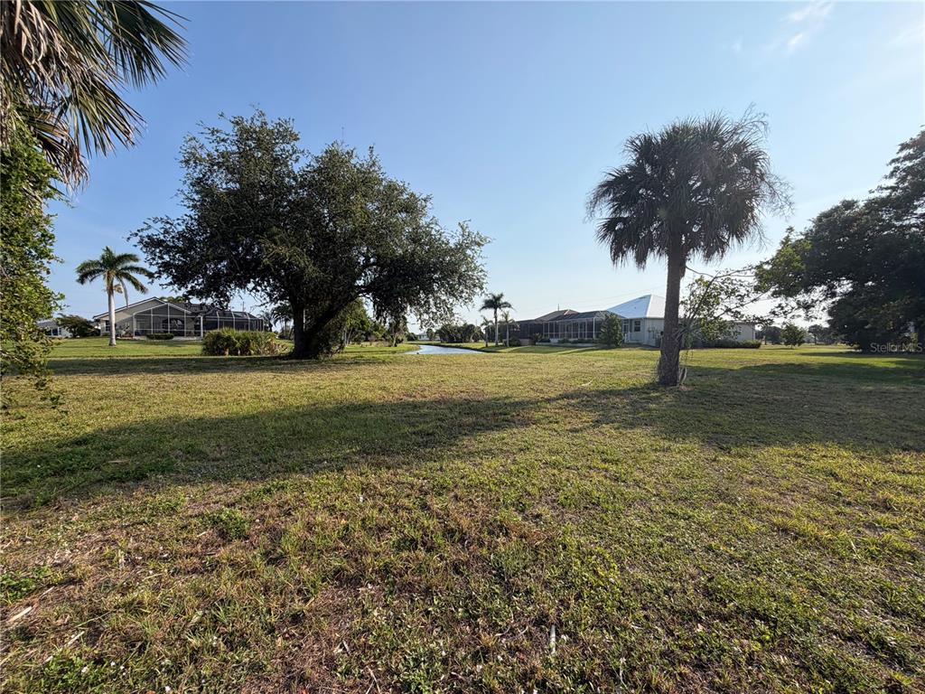 A grassy lot features several palm trees, a large oak tree, and a distant canal — 24360 SAN RAFAEL ROAD, PUNTA GORDA, FL