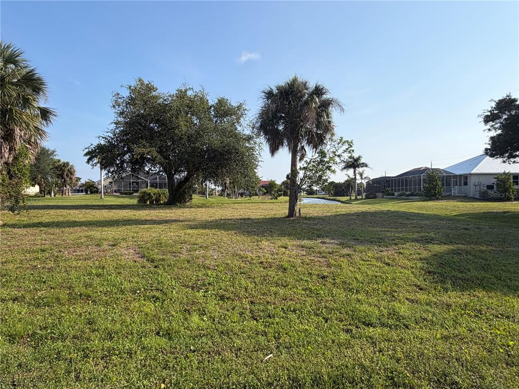 A grassy vacant lot features several palm and oak trees with a canal in the background — 24360 SAN RAFAEL ROAD, PUNTA GORDA, FL