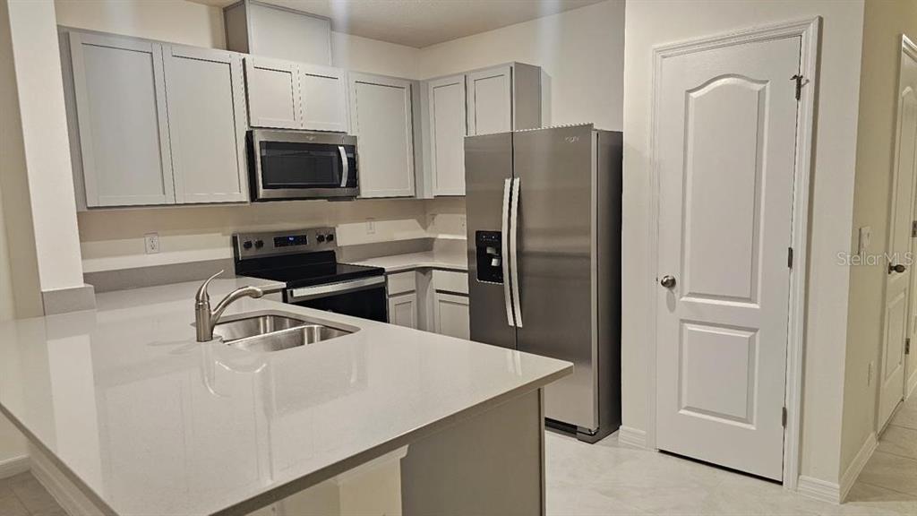 A kitchen features light gray cabinets, stainless steel appliances, and a white quartz countertop island — 1975 TAMARACK PASS, DAVENPORT, FL