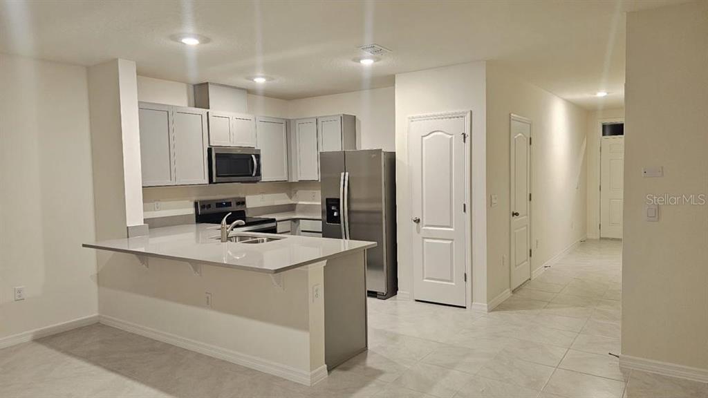 A kitchen features light gray cabinets, stainless steel appliances, and a white quartz island — 1975 TAMARACK PASS, DAVENPORT, FL