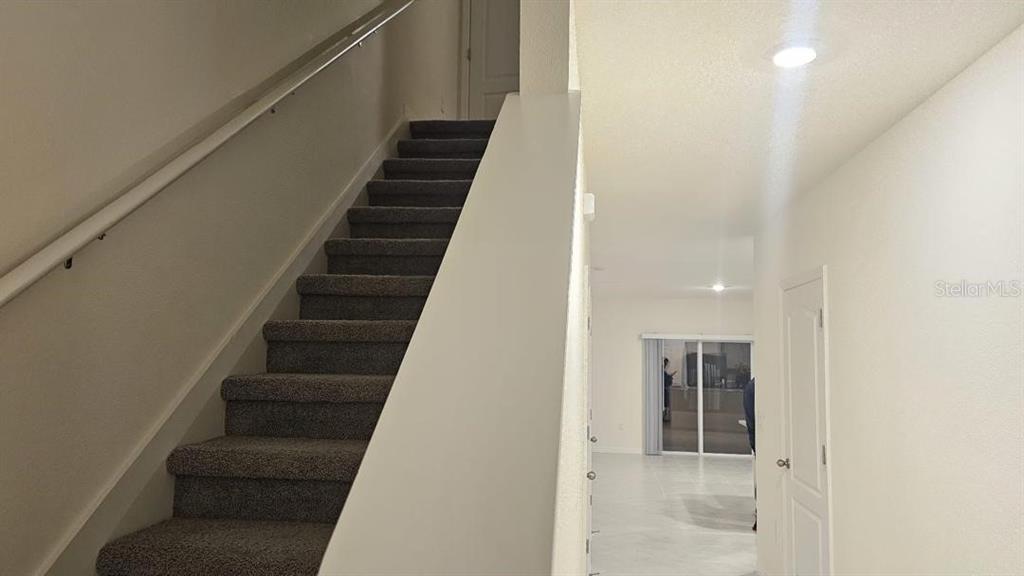 A carpeted staircase with a handrail leads upward next to a hallway with tile flooring — 1975 TAMARACK PASS, DAVENPORT, FL