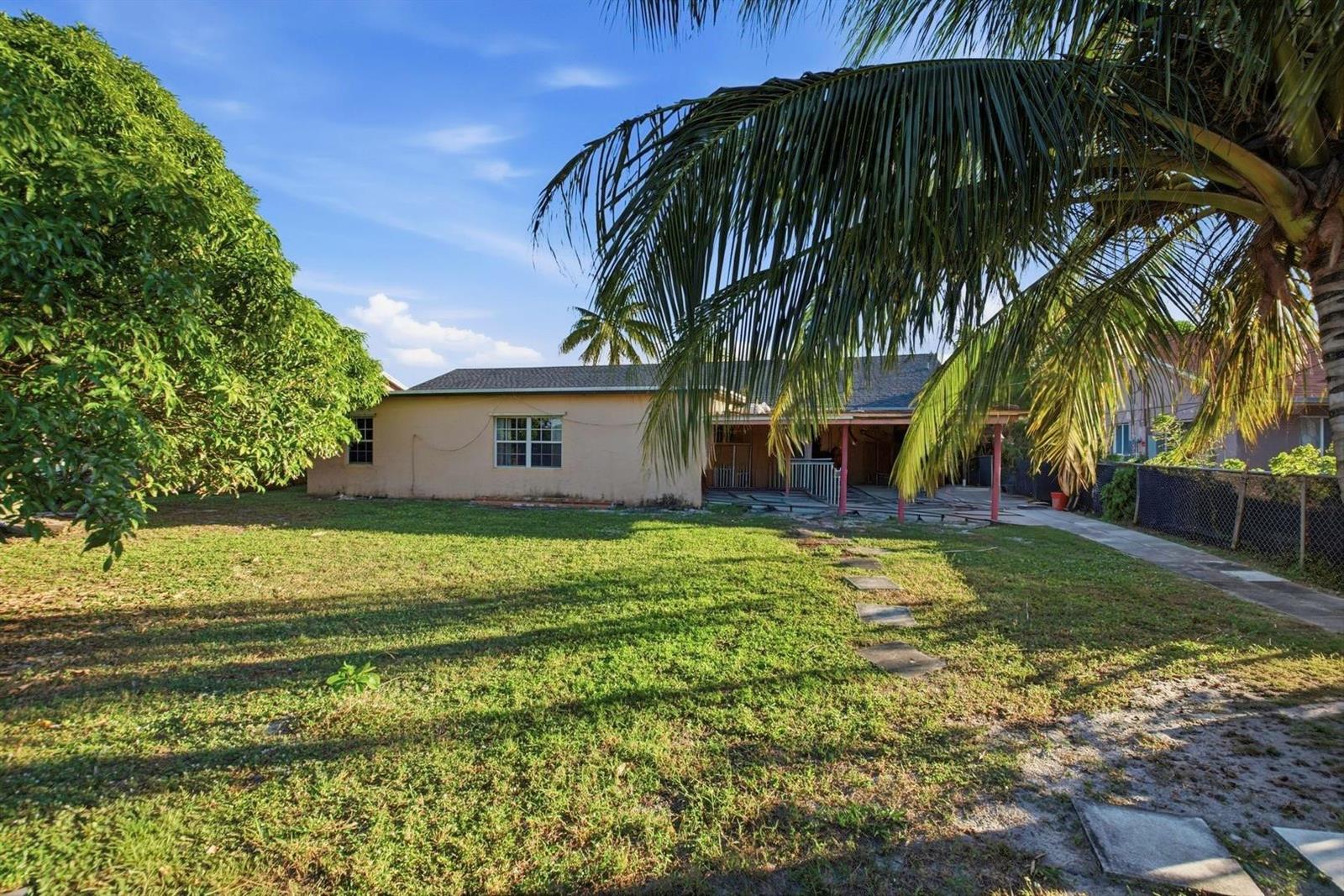 The backyard of a single-story house features a grassy lawn, a patio, and palm trees — 561 NE 38th Street, Deerfield Beach FL 33064, DEERFIELD BEACH, FL