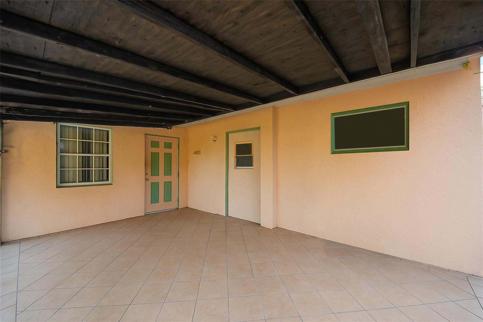 A covered patio with tiled flooring, two doors, a window, and a dark wooden ceiling — 561 NE 38th Street, Deerfield Beach FL 33064, DEERFIELD BEACH, FL