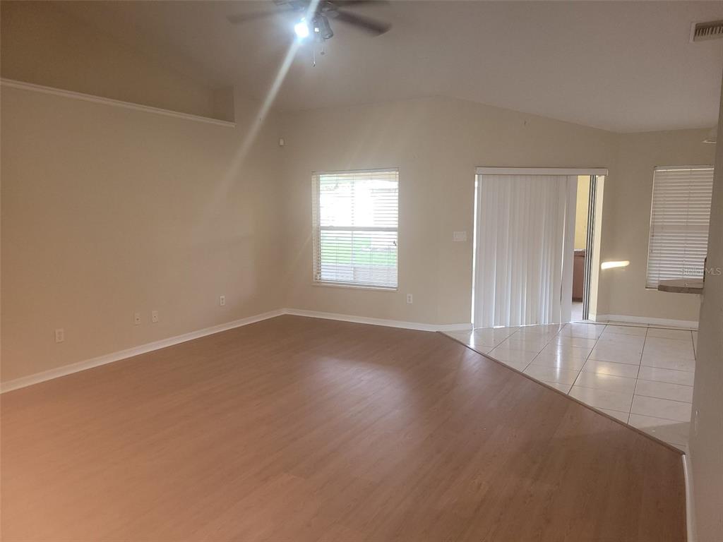 An open-concept living room features light wood-look flooring, beige walls, and a sliding glass door — 4650 NE 16TH PLACE, OCALA, FL