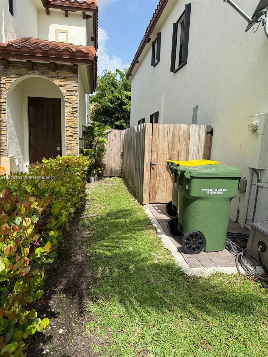 A narrow side yard features a green trash bin, a wooden fence, and landscaping — 156 NE 24th Ave, Homestead FL 33033, HOMESTEAD, FL