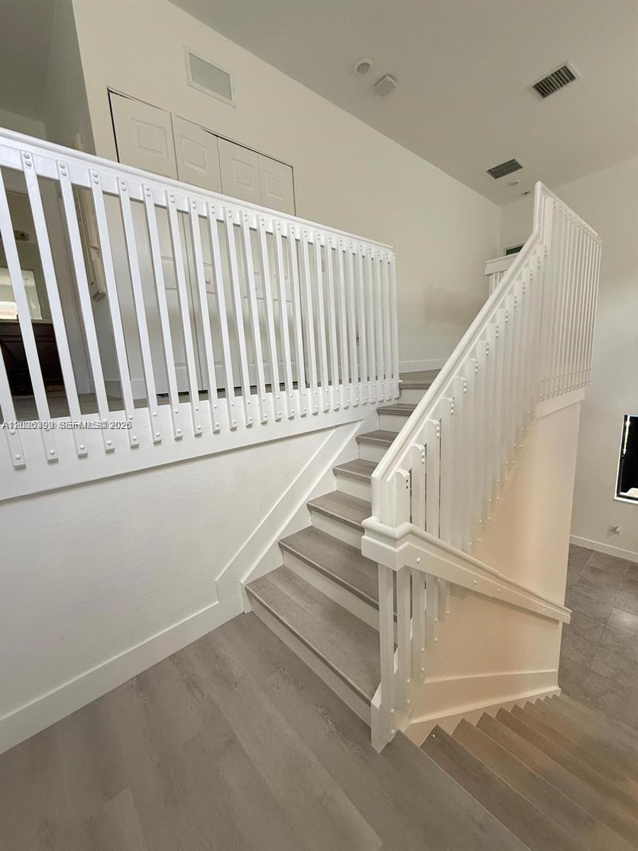 A staircase with white railings and light wood-look flooring leads to an upper level — 156 NE 24th Ave, Homestead FL 33033, HOMESTEAD, FL