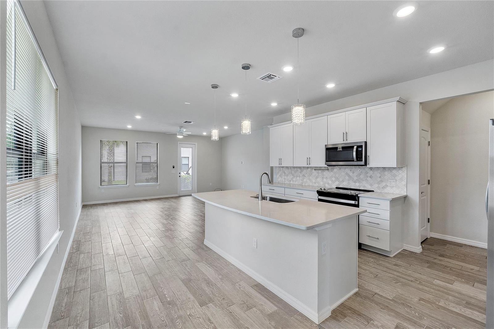 A modern kitchen with white cabinets, a quartz island, and light wood-look flooring — 4851 Indio Trail, Lake Worth FL 33467, LAKE WORTH, FL