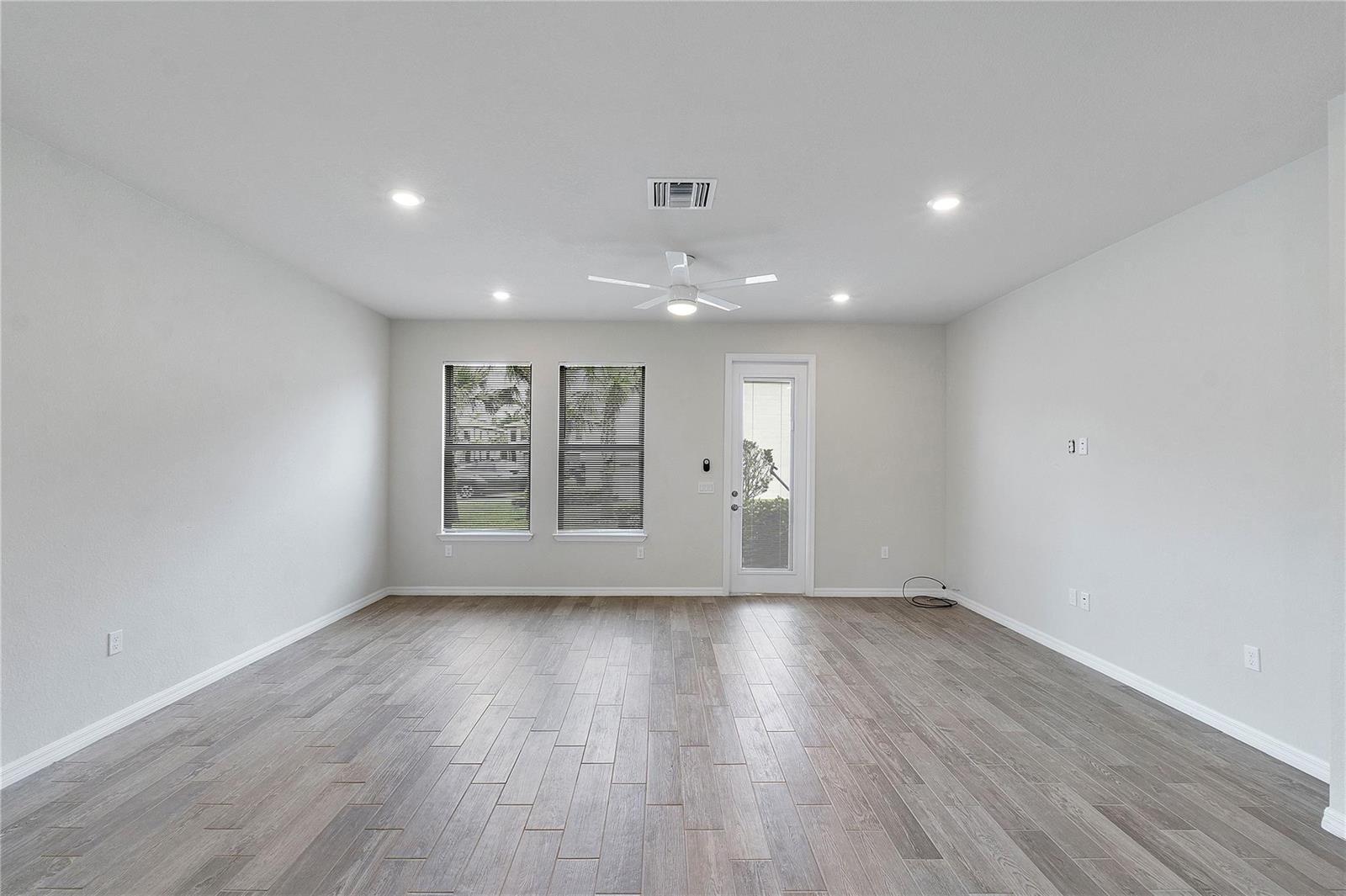 A bright, empty living room features light gray walls, wood-look tile flooring, and a ceiling fan — 4851 Indio Trail, Lake Worth FL 33467, LAKE WORTH, FL