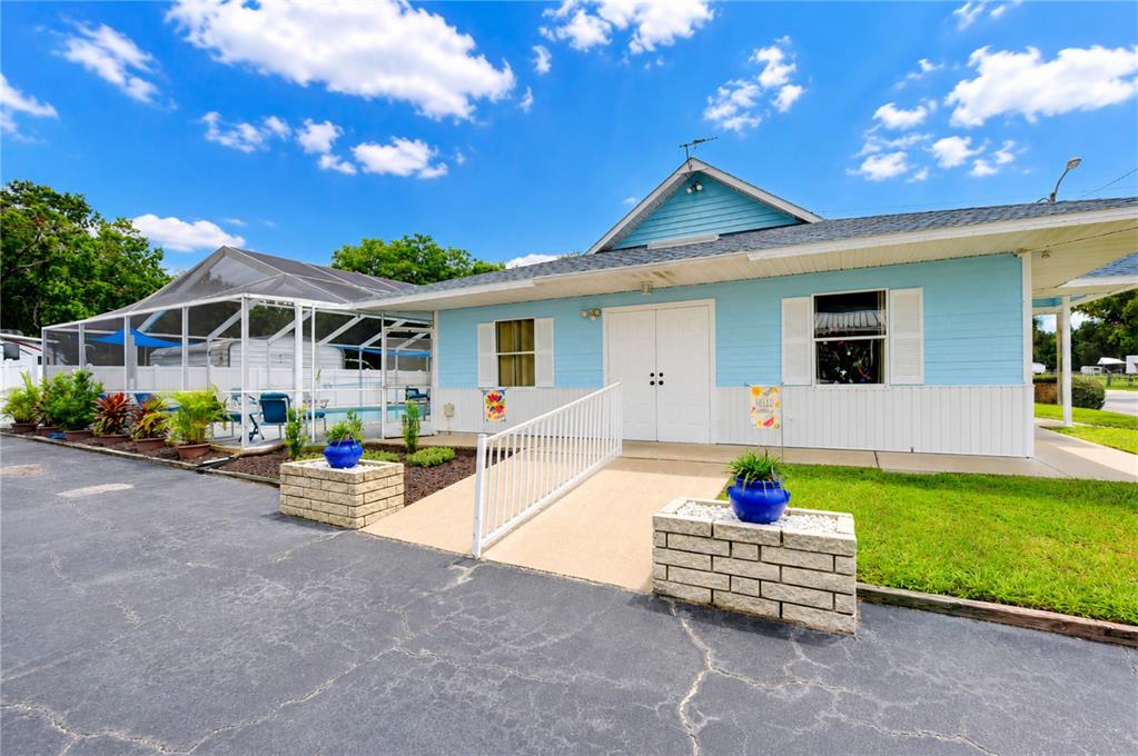 A light blue building features a wheelchair ramp, a screened-in pool area, and brick planters — 34910 HAPPINESS WAY, ZEPHYRHILLS, FL
