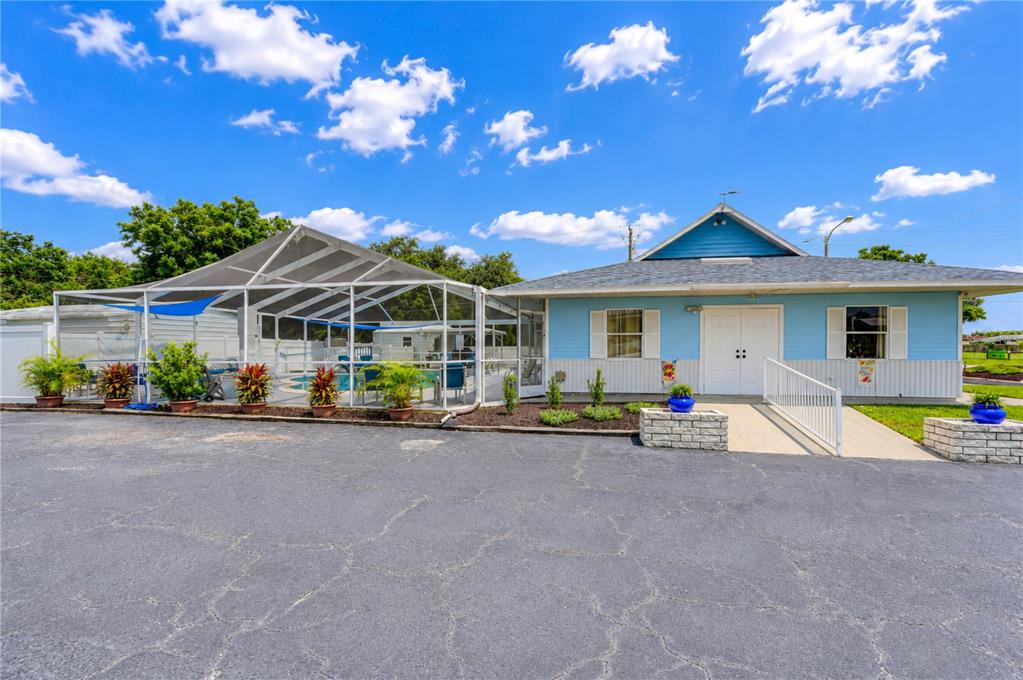 A blue building with a screened-in pool area sits next to a paved parking lot — 34910 HAPPINESS WAY, ZEPHYRHILLS, FL