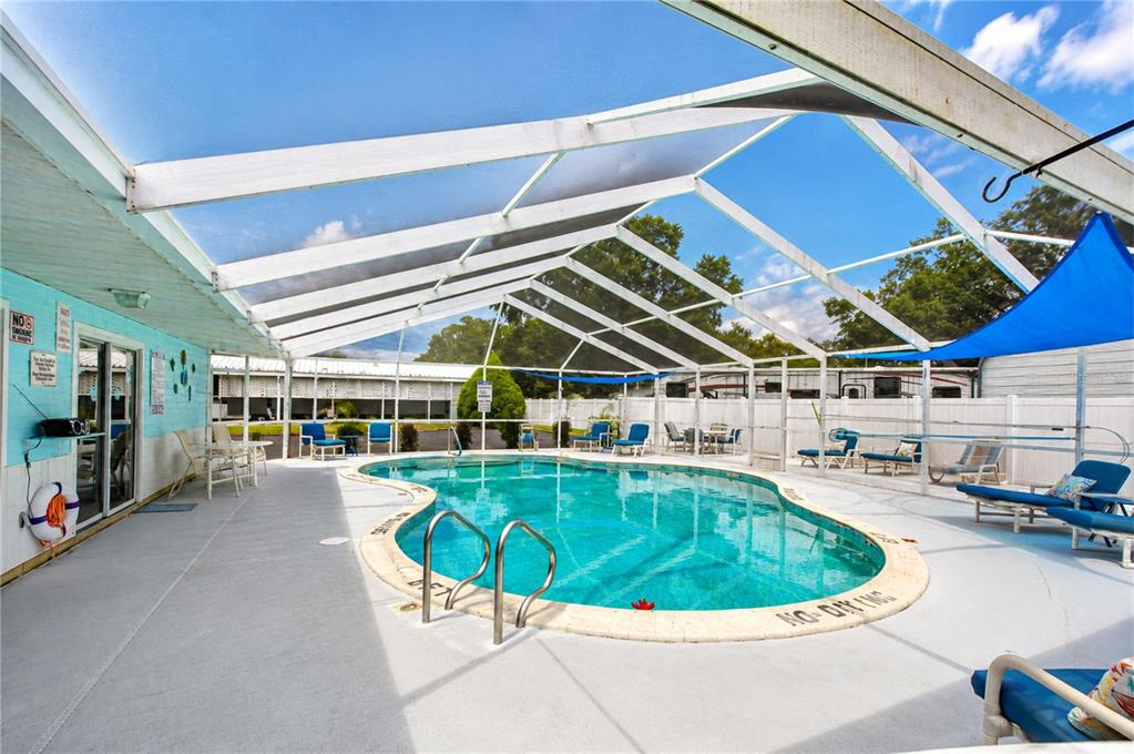 An outdoor swimming pool is enclosed by a white screen structure with surrounding lounge chairs — 34910 HAPPINESS WAY, ZEPHYRHILLS, FL