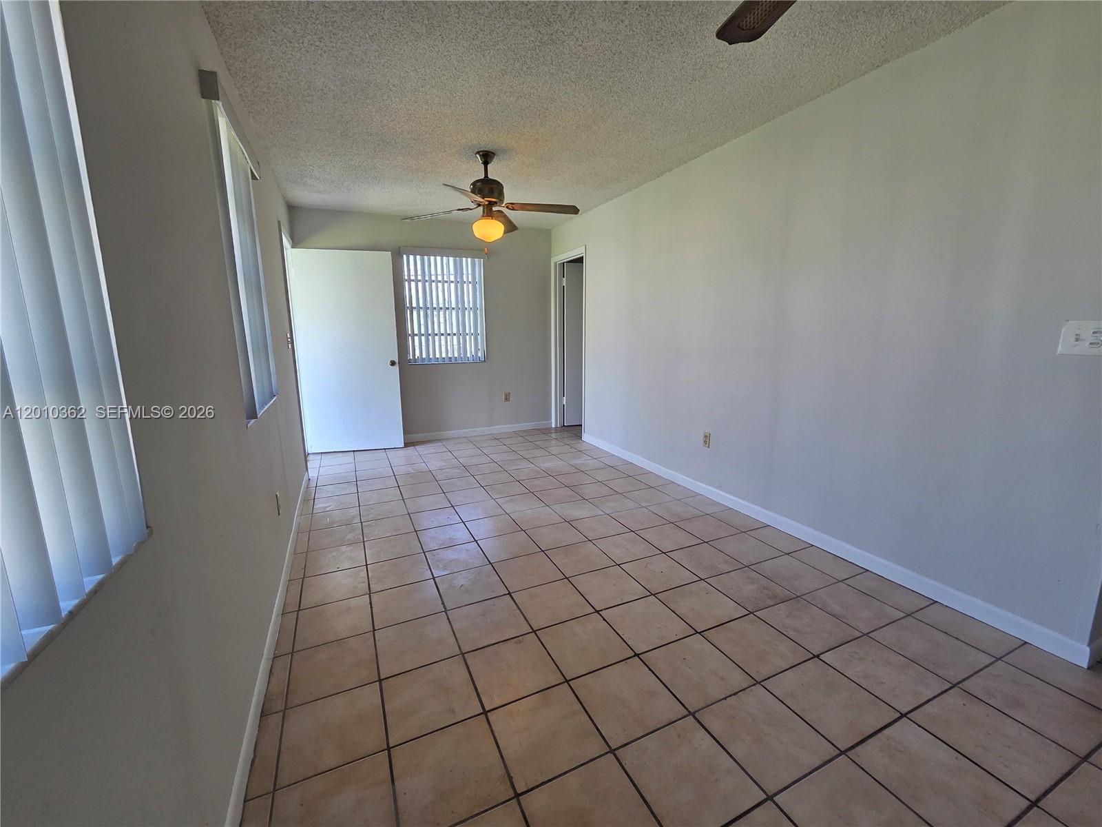 An empty room features light-colored tile flooring, a ceiling fan, and vertical window blinds — 11035 SW 56th St # B, Miami FL 33165, MIAMI, FL