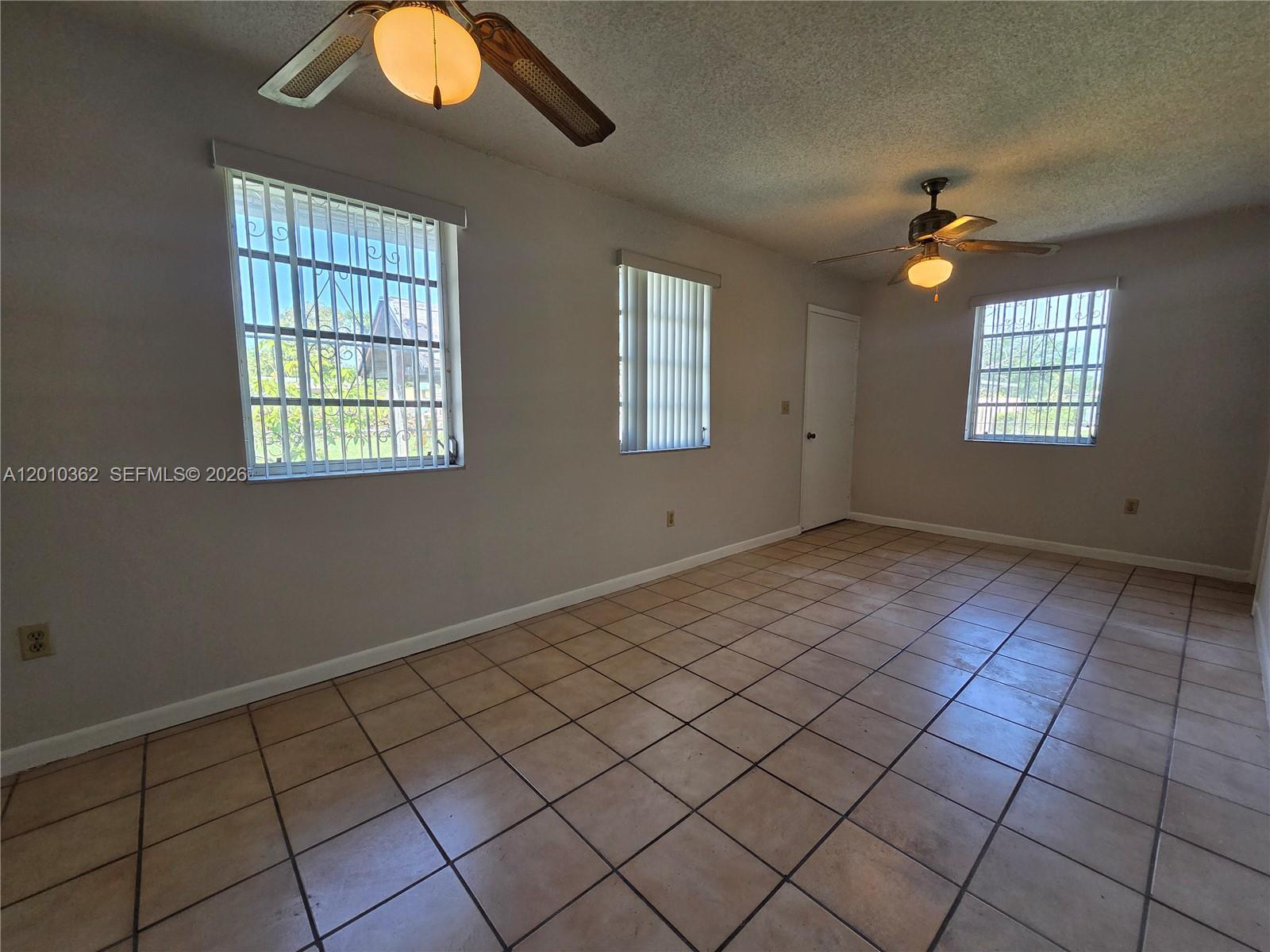 An empty room features tiled floors, two ceiling fans, and windows with security bars — 11035 SW 56th St # B, Miami FL 33165, MIAMI, FL