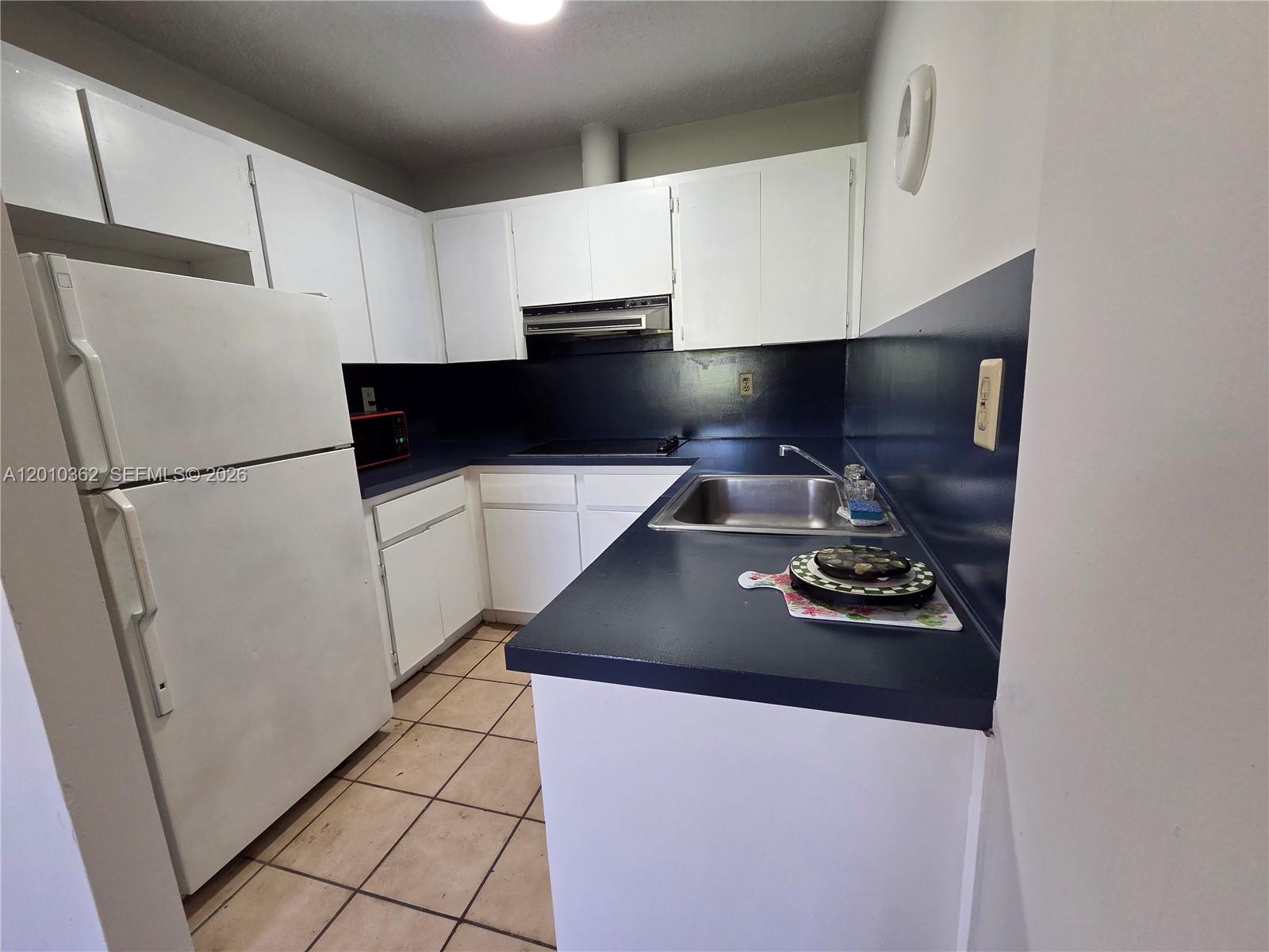 A kitchen features white cabinets, a dark blue countertop, a stainless steel sink, and tile flooring — 11035 SW 56th St # B, Miami FL 33165, MIAMI, FL