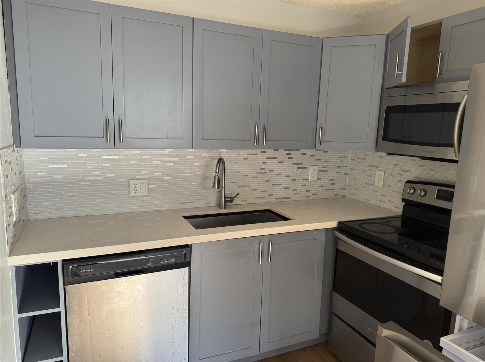 A kitchen features gray cabinets, stainless steel appliances, a white countertop, and a tiled backsplash — 1503 N J Street # A, FL 33460, FL