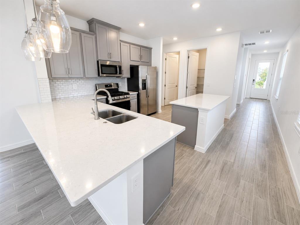 A kitchen features gray cabinets, white countertops, a large island, and light wood-look tile flooring — 994 TEAL CREEK DRIVE, ST CLOUD, FL