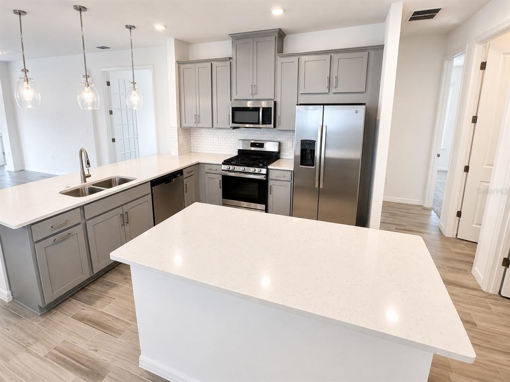 A modern kitchen features gray cabinets, white quartz countertops, stainless steel appliances, and a central island — 994 TEAL CREEK DRIVE, ST CLOUD, FL