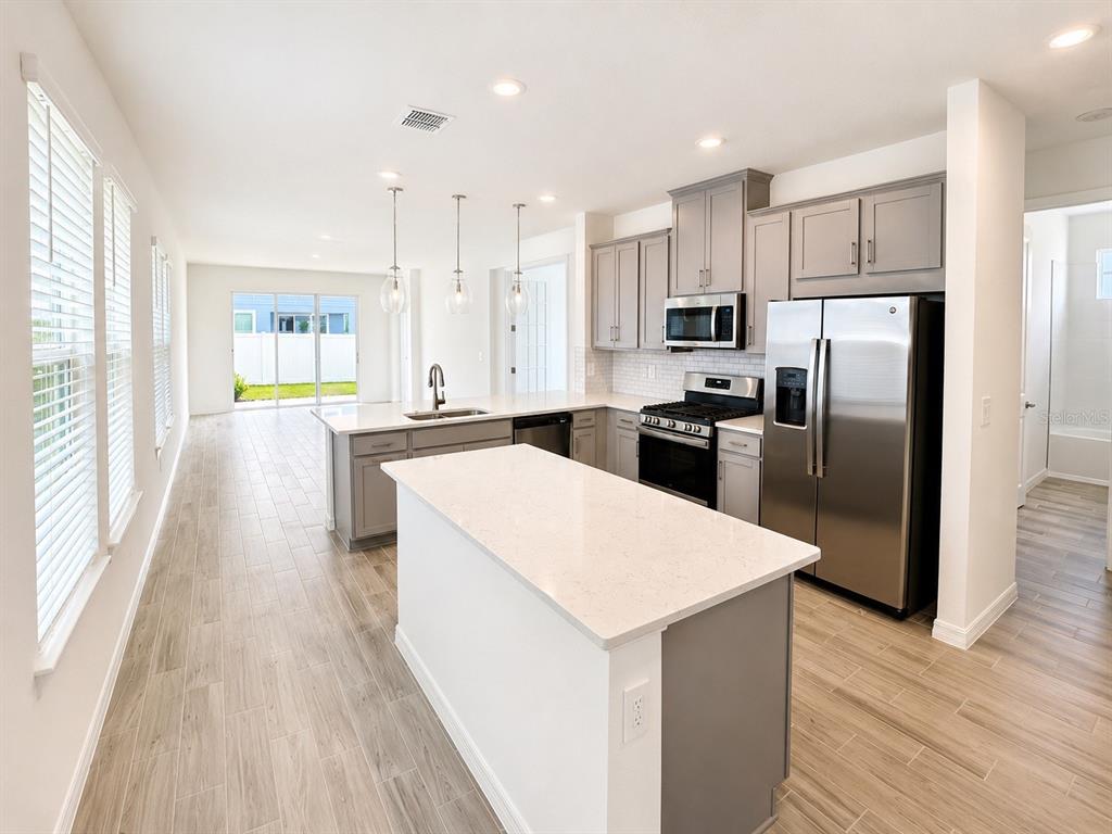 A modern kitchen features gray cabinets, stainless steel appliances, a white island, and wood-look flooring — 994 TEAL CREEK DRIVE, ST CLOUD, FL