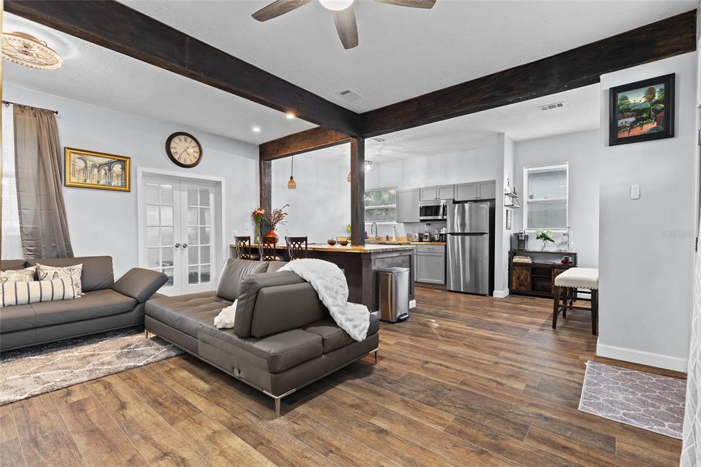 An open-concept living room and kitchen featuring dark wood beams, leather sofas, and wood flooring — 234 W MAGNOLIA STREET, APOPKA, FL