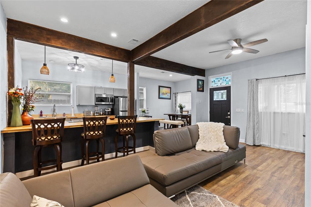 An open-concept living room and kitchen featuring dark wood beams, bar seating, and leather sofas — 234 W MAGNOLIA STREET, APOPKA, FL
