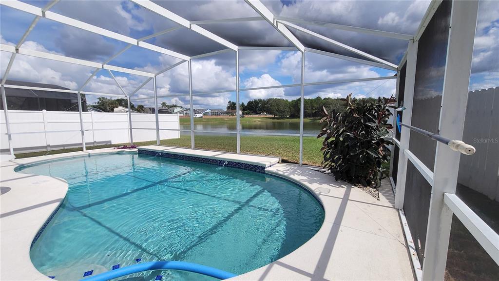 A screened-in swimming pool overlooks a lake behind a white vinyl fence — 3011 BRANSBURY COURT, KISSIMMEE, FL