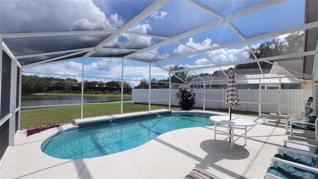 A screened-in swimming pool patio overlooks a lake with a white fence in the background — 3011 BRANSBURY COURT, KISSIMMEE, FL