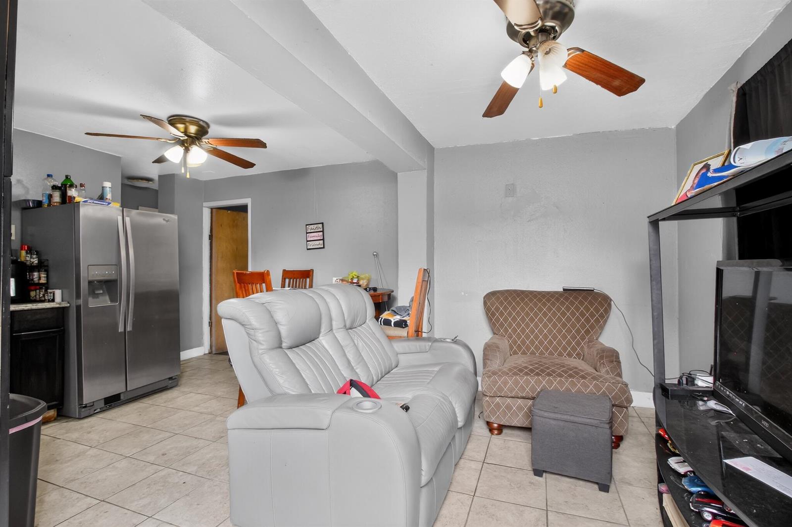 A living room with tile flooring, a light gray sofa, a brown armchair, and a kitchen — 608 NW 15th Avenue, Pompano Beach FL 33069, POMPANO BEACH, FL