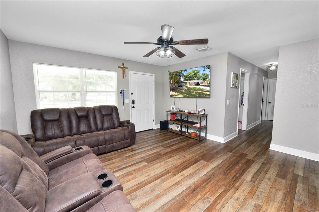 A living room features wood-look flooring, a brown reclining sofa, a ceiling fan, and a television — 4561 DAVID DRIVE, BARTOW, FL