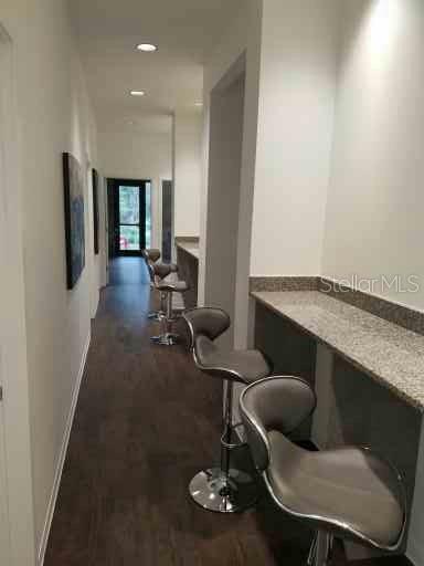 A hallway features a long granite countertop with three modern bar stools and dark flooring — 2298 COLBERT LANE, PALM COAST, FL