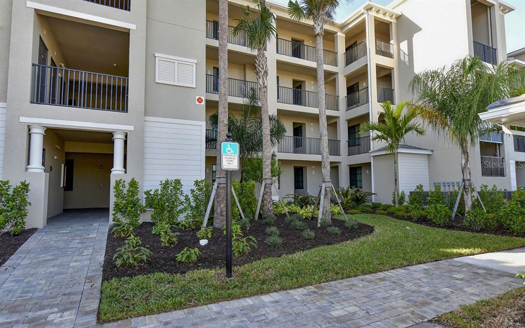 A multi-story apartment building exterior with a paved walkway, palm trees, and a handicap sign — 17626 GAWTHROP DRIVE UNIT 206, BRADENTON, FL