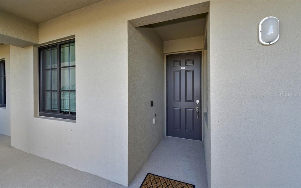 A dark gray front door is recessed into a beige stucco exterior wall — 17626 GAWTHROP DRIVE UNIT 206, BRADENTON, FL