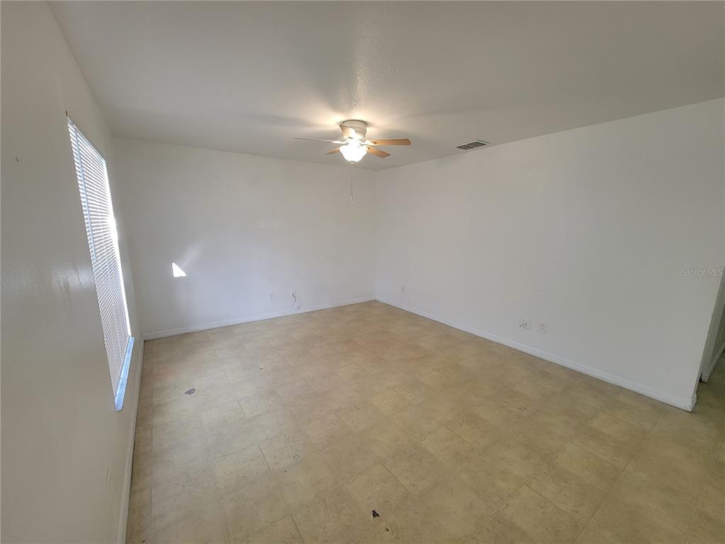 An empty room features white walls, a ceiling fan, and light-colored square floor tiles — 15755 SW 33RD AVE ROAD UNIT 1, OCALA, FL