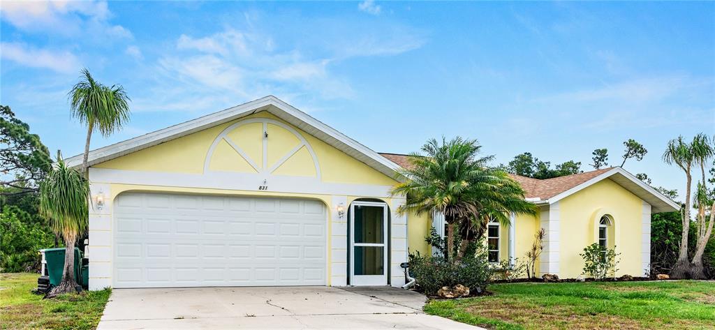 A yellow single-story house features a two-car garage, a front entrance, and several palm trees — 831 COLUMBIA STREET, PORT CHARLOTTE, FL