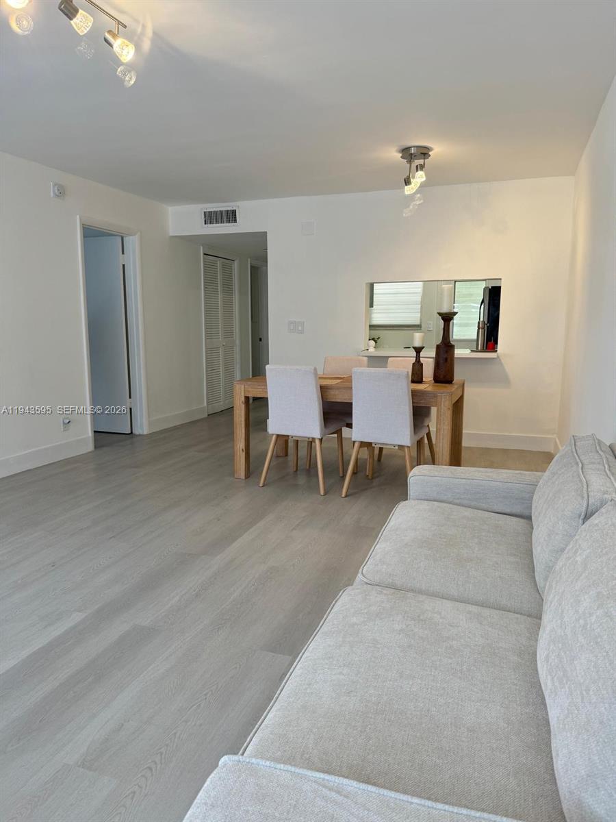 A living room with light wood-look flooring features a dining table and a grey sofa — 330 SE 2nd St # 104F, Hallandale Beach FL 33009, HALLANDALE BEACH, FL