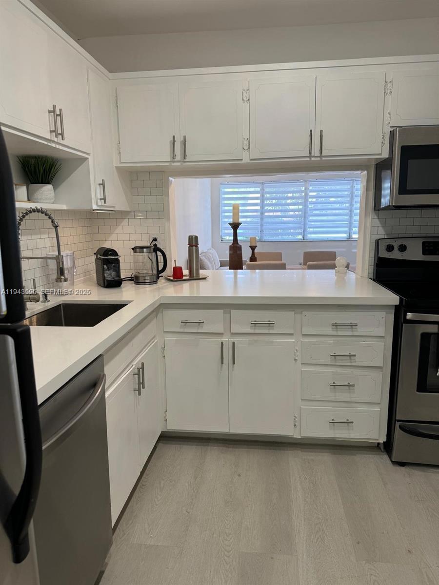 A kitchen features white cabinets, a white countertop, stainless steel appliances, and a subway tile backsplash — 330 SE 2nd St # 104F, Hallandale Beach FL 33009, HALLANDALE BEACH, FL