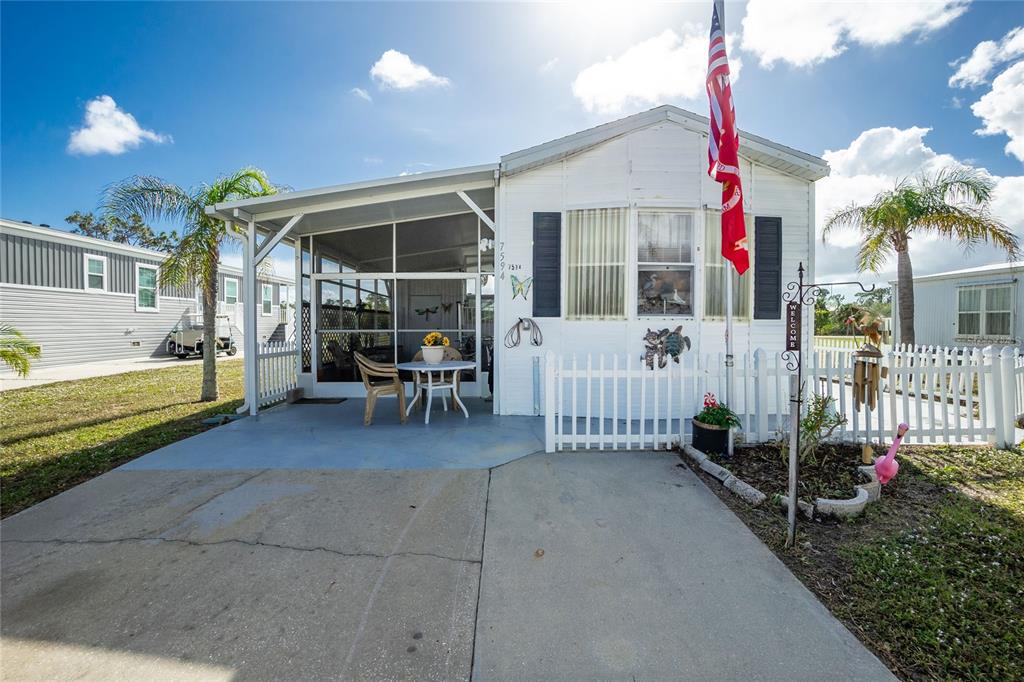 A white mobile home features a screened-in porch, a concrete driveway, and a small picket fence — 7594 RATAN CIRCLE, PORT CHARLOTTE, FL