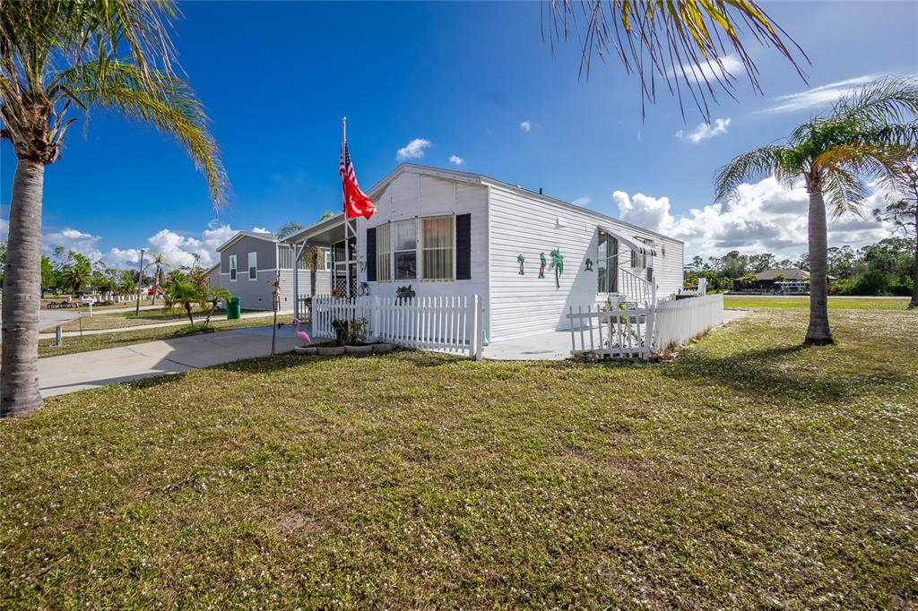 A white mobile home with a fenced patio and an American flag stands on grass — 7594 RATAN CIRCLE, PORT CHARLOTTE, FL