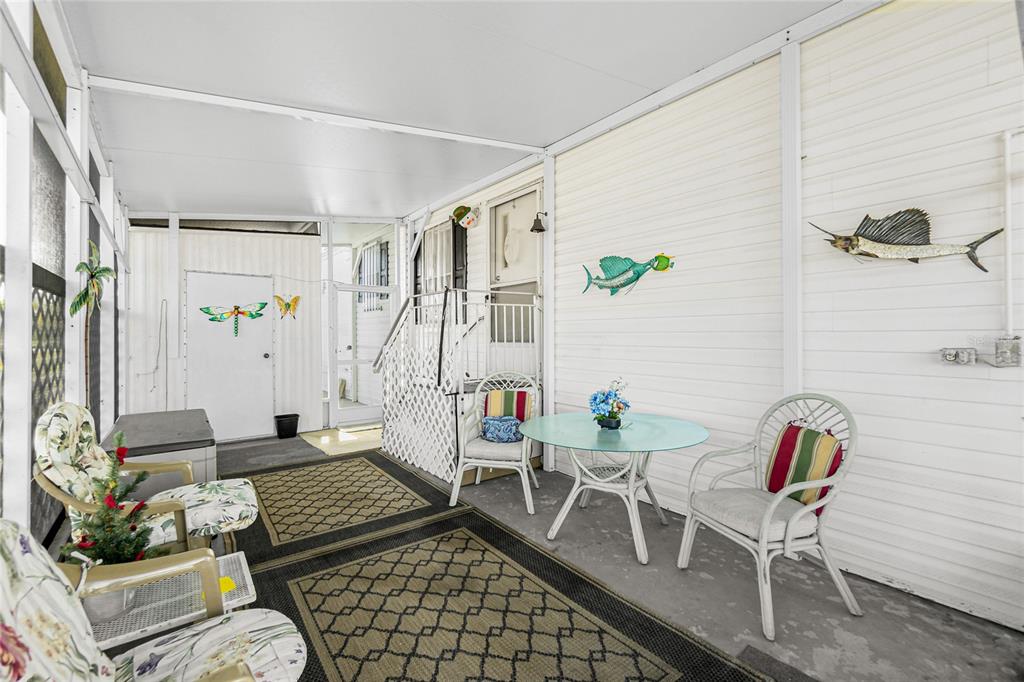 A screened-in porch features white siding, outdoor furniture, patterned rugs, and decorative wall-mounted fish art — 7594 RATAN CIRCLE, PORT CHARLOTTE, FL