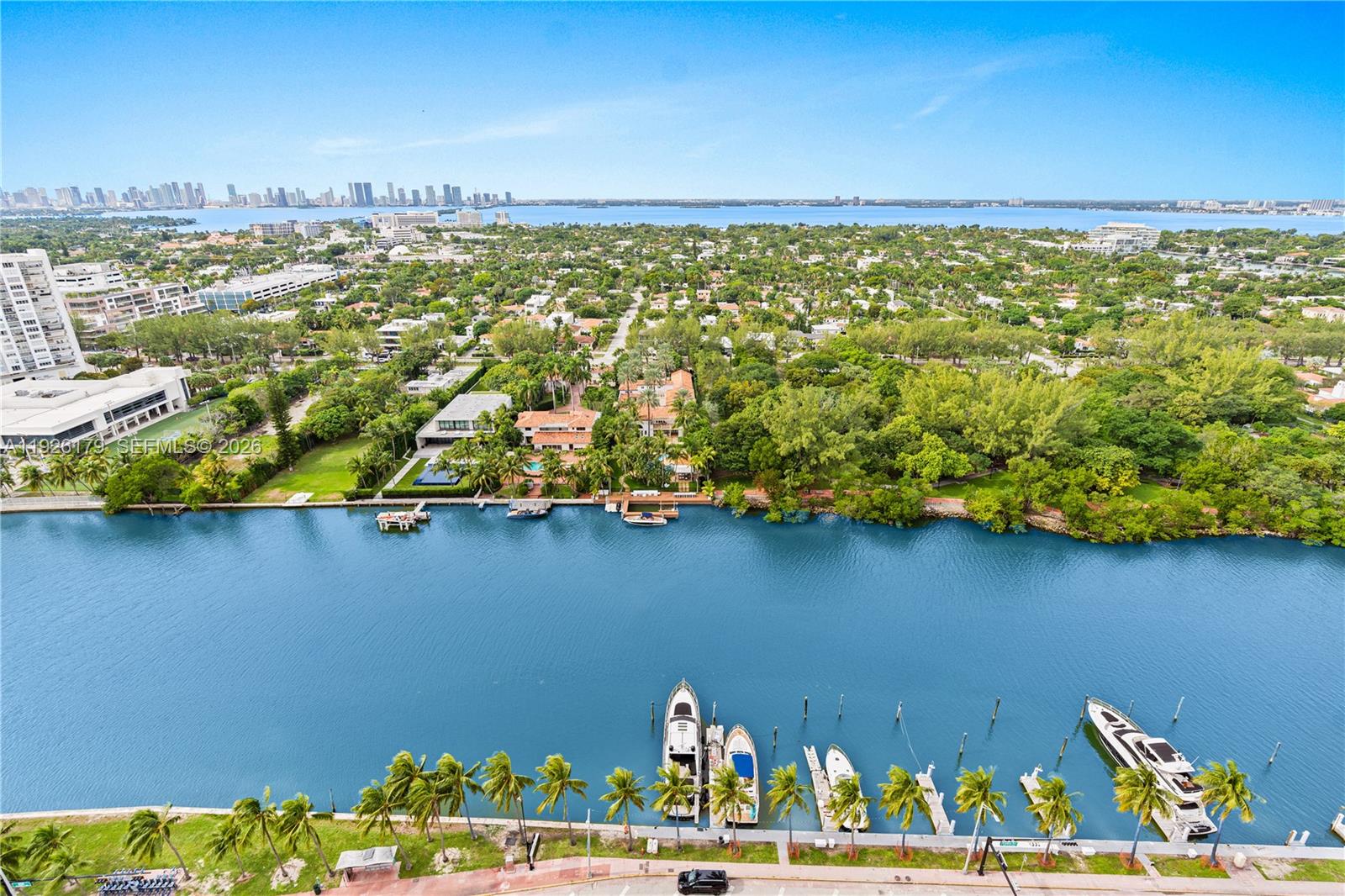An aerial view shows a canal with docked boats, lush greenery, and a distant city skyline — 4401 Collins Ave # 2517, Miami Beach FL 33140, MIAMI BEACH, FL