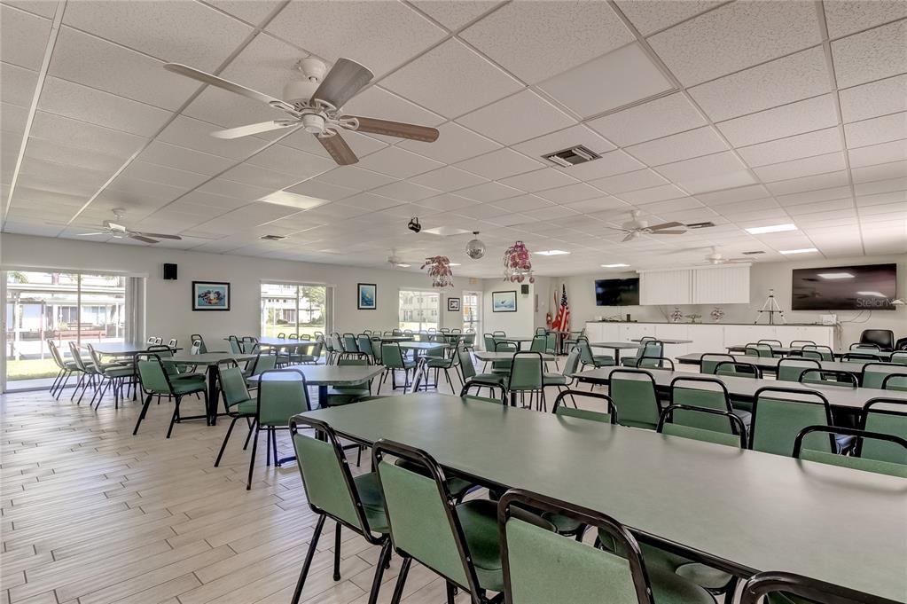 A large community room features rows of tables with green chairs and ceiling fans — 4890 BAY STREET NE UNIT 323, ST PETERSBURG, FL