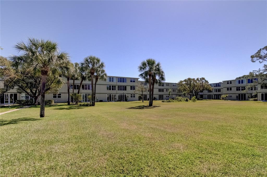A multi-story apartment complex sits behind a large, grassy lawn with several palm trees — 4890 BAY STREET NE UNIT 323, ST PETERSBURG, FL