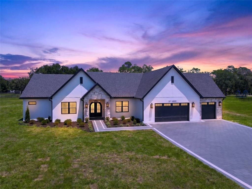 A modern white house with a stone entryway, black trim, and a paved driveway — 14800 MIM PLACE, DADE CITY, FL