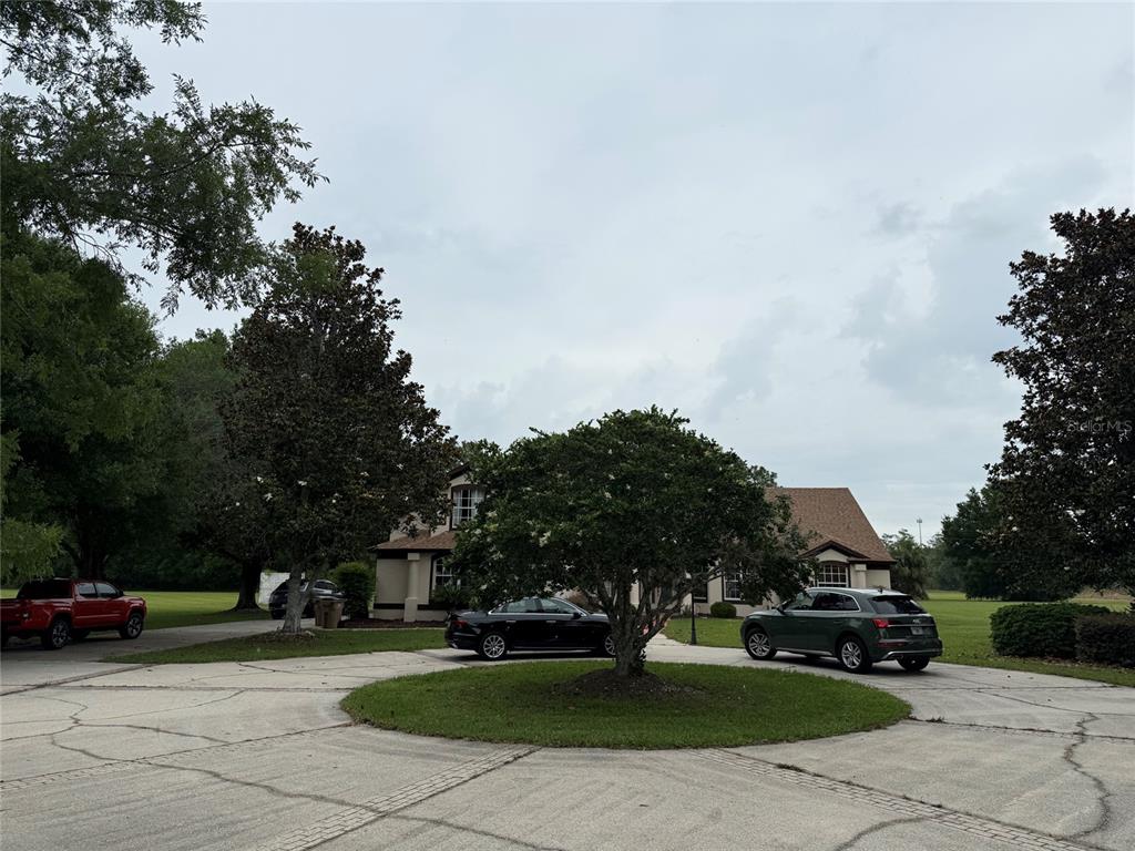 A circular driveway surrounds a central tree in front of a house with three vehicles — 31405 BEAR POND DRIVE, SORRENTO, FL