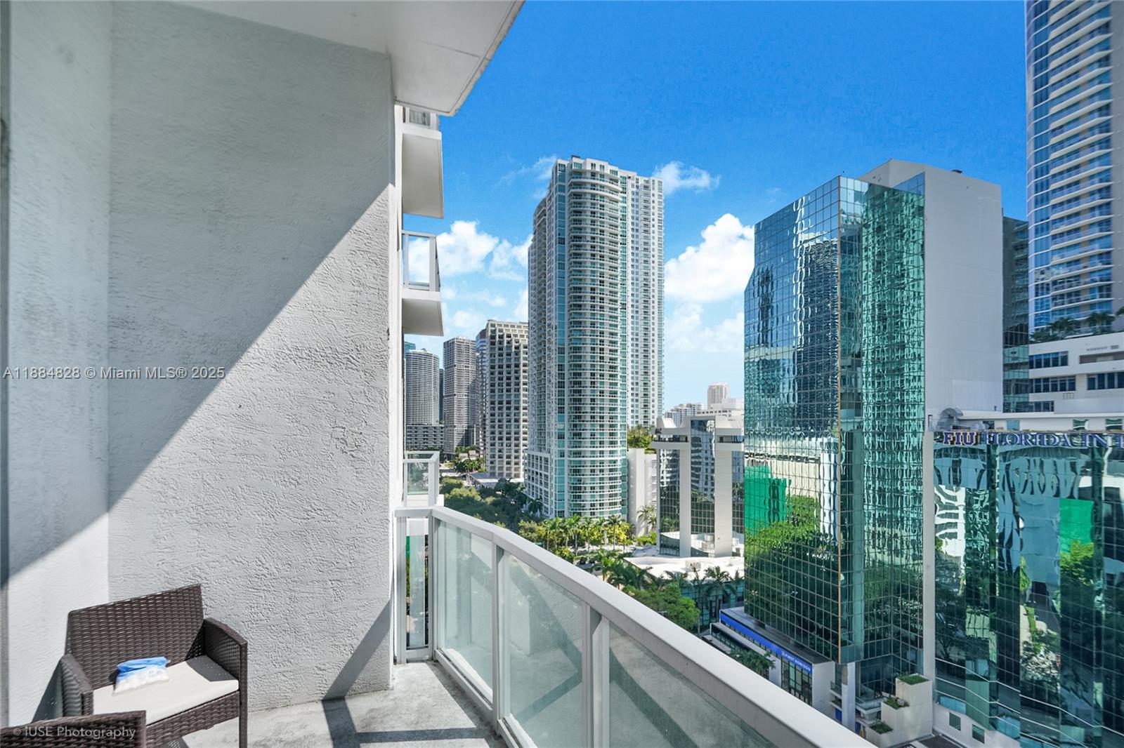 A balcony with a wicker chair overlooks a dense urban skyline of glass skyscrapers — 1060 Brickell Ave # 1203, Miami FL 33131, MIAMI, FL