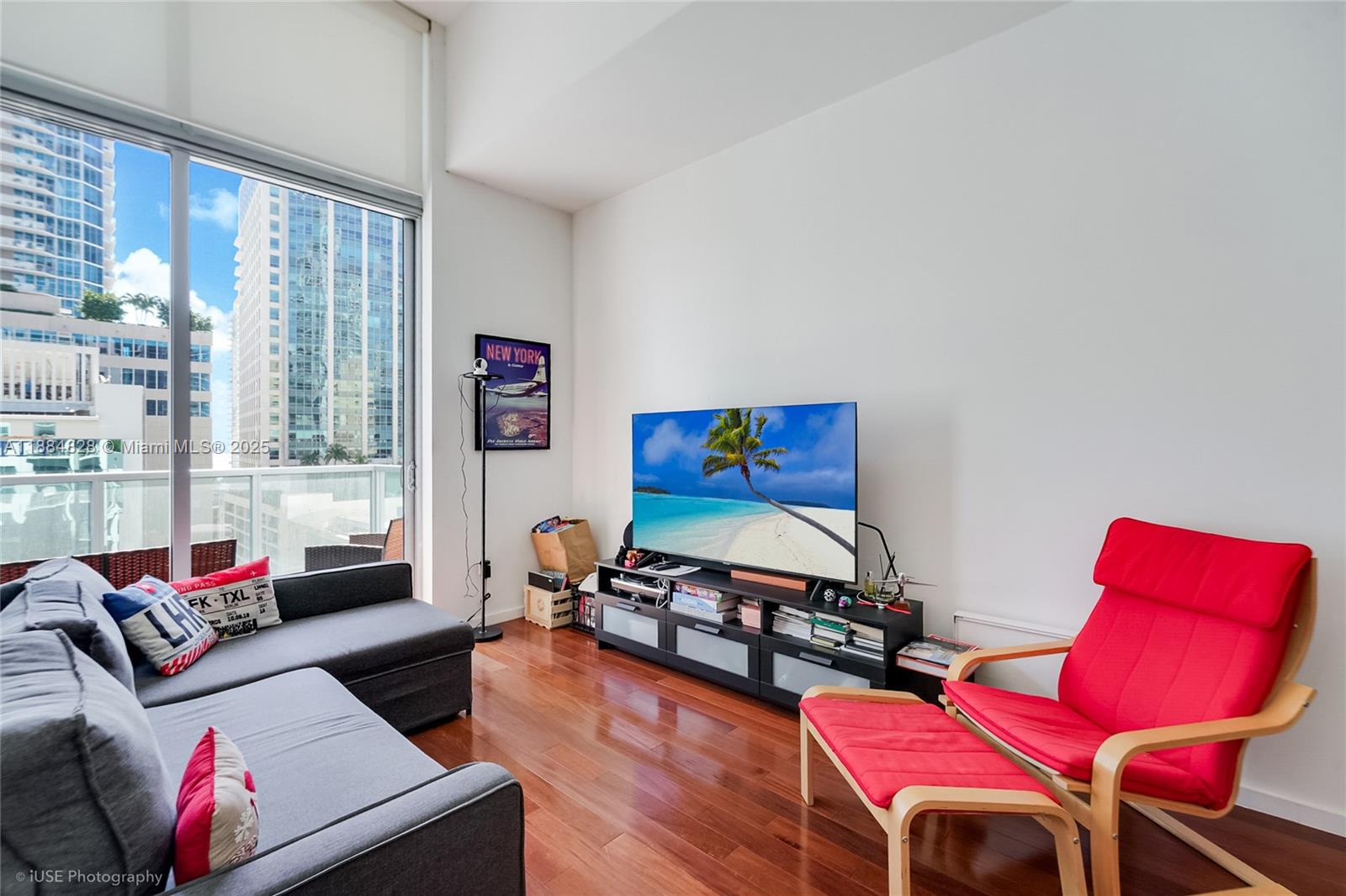 A living room features a grey sofa, a red armchair, and a television on a stand — 1060 Brickell Ave # 1203, Miami FL 33131, MIAMI, FL