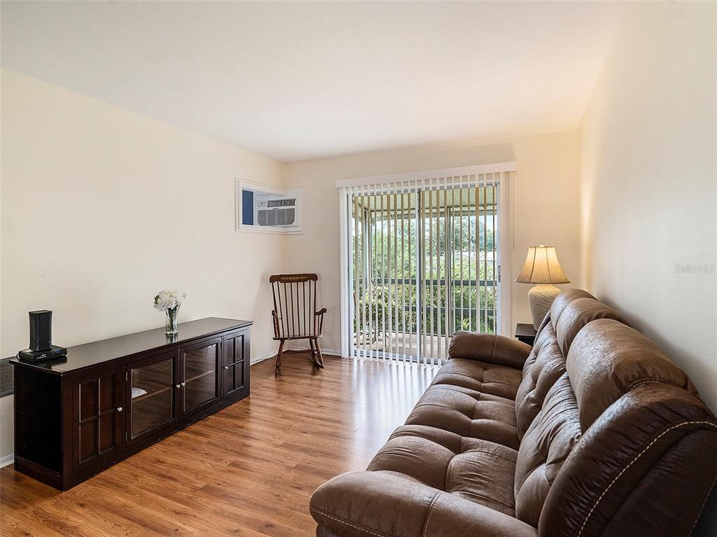 A living room features wood-look flooring, a brown sofa, a media console, and sliding glass doors — 1859 RESTFUL DRIVE UNIT L26, BRADENTON, FL